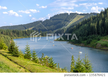 Mountain lake with paddle boats and pine slopes. Summer leisure on water. 135876421