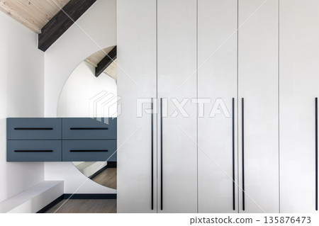 Bright wardrobe with tall black handles and round mirror. Minimal interior. Bright wardrobe with tall black handles and round mirror. Minimal interior. 135876473
