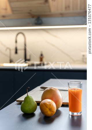 Carrot juice glass with citrus by cutting board in stylish kitchen. Vitamin mood. Carrot juice glass with citrus by cutting board in stylish kitchen. Vitamin mood. 135876477
