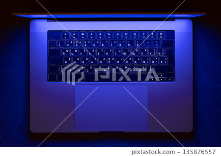 Laptop keyboard in blue neon glow. Night cyber office. 135876557