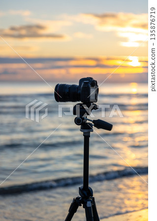 Tripod with camera on sand in golden light by the seaside. Camera and tripod, beach. Tripod with camera on sand in golden light by the seaside. Camera and tripod, beach. 135876719