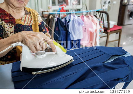 Senior citizens ironing student skirt and clothing in a house. Senior citizens ironing student skirt and clothing in a house. 135877139