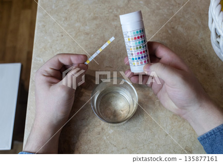 A man in the kitchen tests tap water quality with a test strip. Home testing for drinking water safety, pH, chlorine, and chemical contaminants. A man in the kitchen tests tap water quality with a test strip. Home testing for drinking water safety, pH, chlorine, and chemical contaminants. 135877161