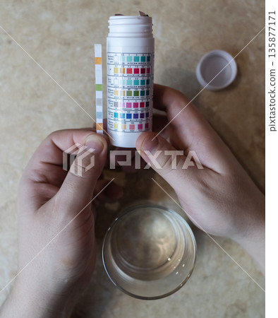 A man in the kitchen tests tap water quality with a test strip. Home testing for drinking water safety, pH, chlorine, and chemical contaminants. A man in the kitchen tests tap water quality with a test strip. Home testing for drinking water safety, pH, chlorine, and chemical contaminants. 135877171