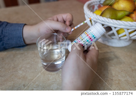 A man in the kitchen tests tap water quality with a test strip. Home testing for drinking water safety, pH, chlorine, and chemical contaminants. A man in the kitchen tests tap water quality with a test strip. Home testing for drinking water safety, pH, chlorine, and chemical contaminants. 135877174