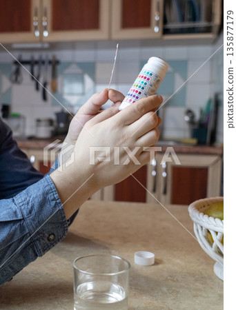 A man in the kitchen tests tap water quality with a test strip. Home testing for drinking water safety, pH, chlorine, and chemical contaminants. 135877179