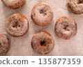 Apple cider or pumpkin spice donuts being covered in cinnamon sugar after baking 135877359