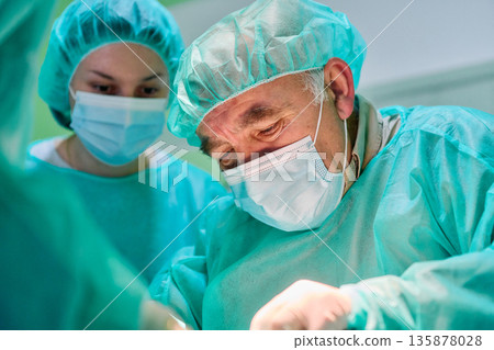 Surgeon in Mask and Cap Performs Surgery with Team in Bright Operating Room 135878028