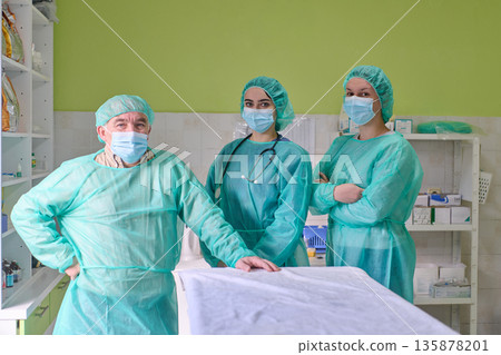 Medical Team in Green Surgical Gowns and Masks Stands by Patient in Operating Room Medical Team in Green Surgical Gowns and Masks Stands by Patient in Operating Room 135878201