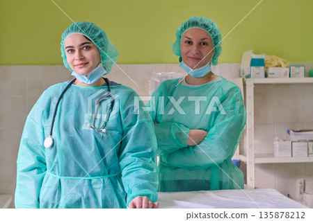 Two Medical Professionals In Green Scrubs And Masks Stand In Clinic Ready To Help 135878212