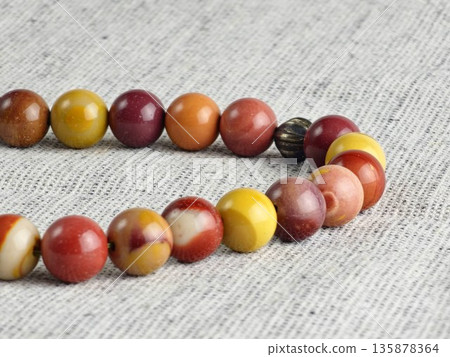 Prayer beads made of mukaite jasper against a burlap background. 33-bead prayer beads are traditionally used for meditation by people of various faiths. Prayer beads made of mukaite jasper against a burlap background. 33-bead prayer beads are traditionally used for meditation by people of various faiths. 135878364