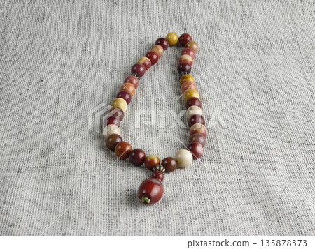 Prayer beads made of mukaite jasper on burlap background. These 33-bead prayer beads are traditionally used in Christian and Islamic prayer practices Prayer beads made of mukaite jasper on burlap background. These 33-bead prayer beads are traditionally used in Christian and Islamic prayer practices 135878373