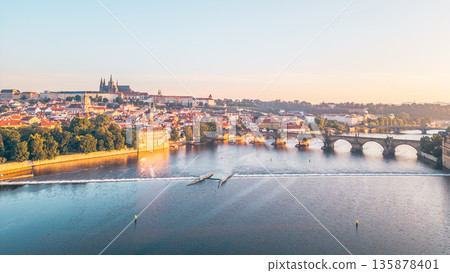 Morning light casts a golden hue over Prague, illuminating the cityscape. The iconic Charles Bridge and Hradcany Castle stand majestically against the dawn sky, reflecting in the Vltava River. Morning light casts a golden hue over Prague, illuminating the cityscape. The iconic Charles Bridge and Hradcany Castle stand majestically against the dawn sky, reflecting in the Vltava River. 135878401