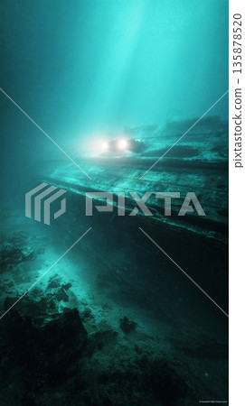 Robotic submersible uses lights to scan wooden hull of ancient galleon underwater. Sand swirls around as it uncovers coral-covered cannons at the site of the wreck 135878520