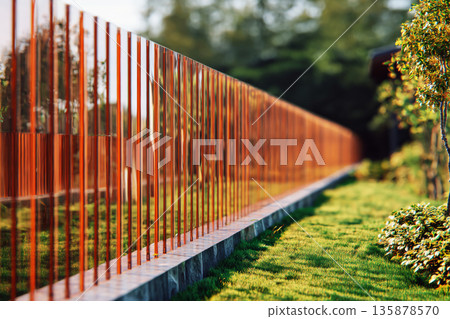 A semi-transparent glass fence marks the boundary of a private garden. The setting is a modern suburban neighborhood with greenery and a home in the background A semi-transparent glass fence marks the boundary of a private garden. The setting is a modern suburban neighborhood with greenery and a home in the background 135878570