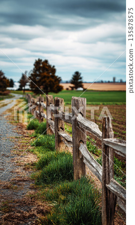 A weathered wooden farm gate stands in front of lush green pasture, surrounded by tall grass and distant hills under a cloudy sky, showing a serene rural scene A weathered wooden farm gate stands in front of lush green pasture, surrounded by tall grass and distant hills under a cloudy sky, showing a serene rural scene 135878575