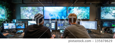 Engineers use touchscreen panels to deploy drones while observing real-time underwater images on large displays in a control room setting focused on a task, banner Engineers use touchscreen panels to deploy drones while observing real-time underwater images on large displays in a control room setting focused on a task, banner 135878629