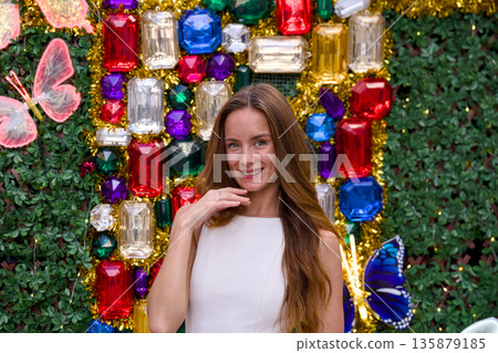 Happy young woman posing at colorful Christmas backdrop with shiny festive gems Happy young woman posing at colorful Christmas backdrop with shiny festive gems 135879185