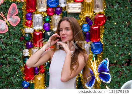 Beautiful young woman posing near colorful Christmas gem wall with festive smile Beautiful young woman posing near colorful Christmas gem wall with festive smile 135879186
