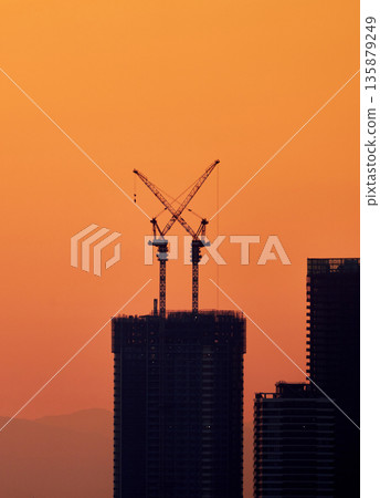 Silhouettes of skyscrapers and construction cranes against the sunset sky 135879249