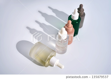 Skincare serum dropper bottles standing with long shadows Skincare serum dropper bottles standing with long shadows 135879537