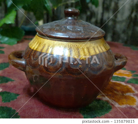 Handmade ceramic pot with lid, made in warm brown and golden shades. Decorated with relief ornament and glazed surface. Traditional tableware in folk style. For themes related to home comfort, cooking Handmade ceramic pot with lid, made in warm brown and golden shades. Decorated with relief ornament and glazed surface. Traditional tableware in folk style. For themes related to home comfort, cooking 135879815