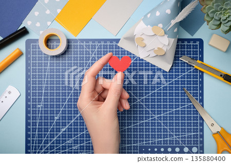 Making a gnome in love. Hand is holding a red paper heart. Creative process. Making a gnome in love. Hand is holding a red paper heart. Creative process. 135880400