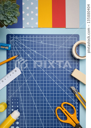 Blue workplace for paper crafts. Knife, ruler, glue, pencil, tape, eraser, cutting mat, colored paper. Place for your text. 135880404