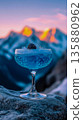A refreshing blue cocktail in a margarita glass with ice and berries on top, standing on rocks in front of snow-covered mountains.	 135880962