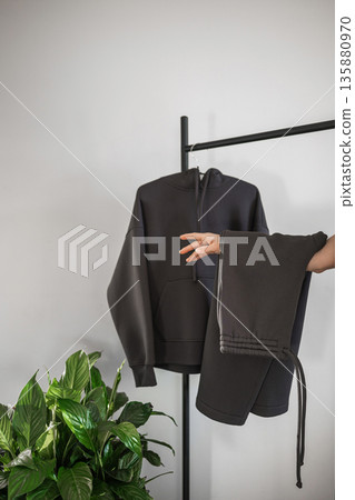 Hoodie and sweatpants displayed on rack with plant in a modern room Hoodie and sweatpants displayed on rack with plant in a modern room 135880970