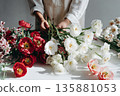 Person arranging flowers at a table in a bright indoor space during daytime 135881053