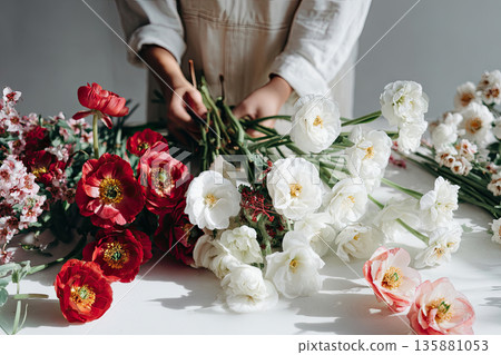 Person arranging flowers at a table in a bright indoor space during daytime 135881053