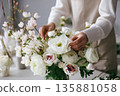 Person arranges flowers in a vase at a table during daytime in a bright space 135881058