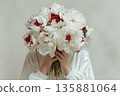 Large bouquet of peonies held by a person in a white top with hands covering the face 135881064