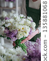 Arranging flowers in a busy shop with various blooms and colors during daytime 135881068