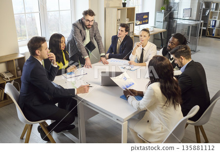 Manager leads office team briefing at table, analyzing charts and strategy Manager leads office team briefing at table, analyzing charts and strategy 135881112