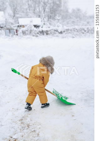 Small child clearing snow with a shovel outdoors during winter, dressed in warm clothing, learning simple work skills and outdoor activity in a snowy environment. Small child clearing snow with a shovel outdoors during winter, dressed in warm clothing, learning simple work skills and outdoor activity in a snowy environment. 135881253