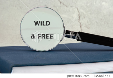 A magnifying glass rests on a dark blue book, clearly showing the bold words Wild and Free beneath its lens 135881355