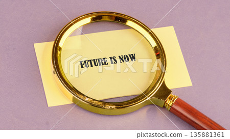 A shiny golden magnifying glass rests on a yellow rectangular paper, clearly showing the bold black words Future Is Now against a soft purple background, emphasizing immediate action 135881361