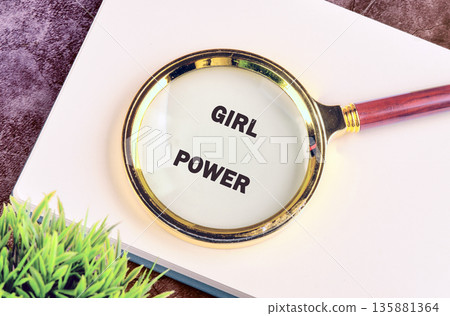 A magnifying glass displays the words Girl Power on a white notebook. A golden rim surrounds the glass, which has a reddish-brown handle 135881364