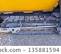 Crawler chassis of a road-building asphalt paver on which layers of bitumen asphalt and gravel mixture have adhered. Road Construction Process, Restoration, Replacement, Outdoor Repair All Year Round 135881594