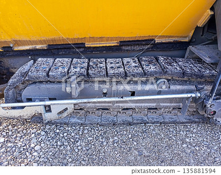 Crawler chassis of a road-building asphalt paver on which layers of bitumen asphalt and gravel mixture have adhered. Road Construction Process, Restoration, Replacement, Outdoor Repair All Year Round 135881594