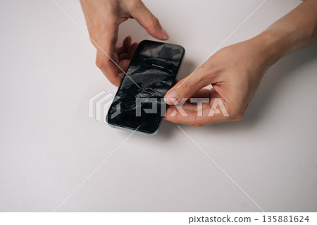 Top view of technician male holding cracked tempered glass screen protector from smartphone. Revealing intact phone screen underneath. Highlighting mobile phone repair and maintenance. Top view of technician male holding cracked tempered glass screen protector from smartphone. Revealing intact phone screen underneath. Highlighting mobile phone repair and maintenance. 135881624