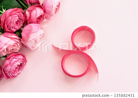 A delicate and creative flat lay celebrating 8 March, International Womens Day. soft pink roses and a ribbon arranged in the shape of 8 on a pastel pink background 135882431