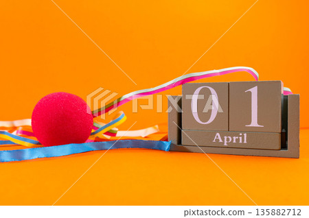 Calendar with clown wig, funny glasses and sequins on brown background. April Fools Day 135882712