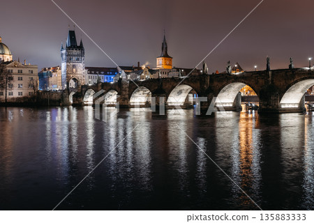 Charles Bridge at Night in Winter Viewed from Lesser Town Riverbank. Vltava River, tourists walking 135883333
