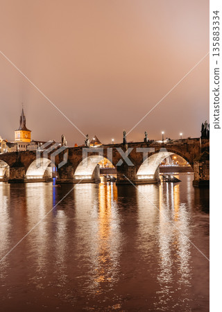 Charles Bridge at Night in Winter Viewed from Lesser Town Riverbank. Vltava River, tourists walking 135883334