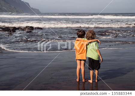 Two Young Boys Hugging on Black Volcanic Beach Facing Atlantic Ocean Two Young Boys Hugging on Black Volcanic Beach Facing Atlantic Ocean 135883344