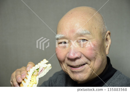 一位老人面帶微笑地吃著熱三明治。 一位老人面帶微笑地吃著熱三明治。 135883568