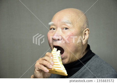 An elderly man eating a hot sandwich with a smile An elderly man eating a hot sandwich with a smile 135883572